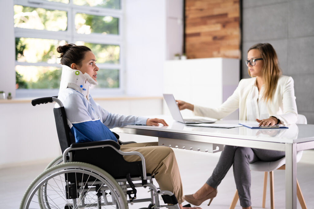 Woman in a neck brace and wheelchair reviewing insurance claim with a female agent