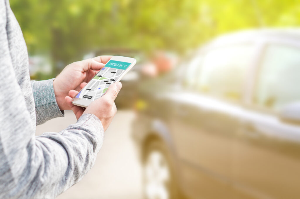 Man holding smartphone looking at a rideshare app with a car in the background