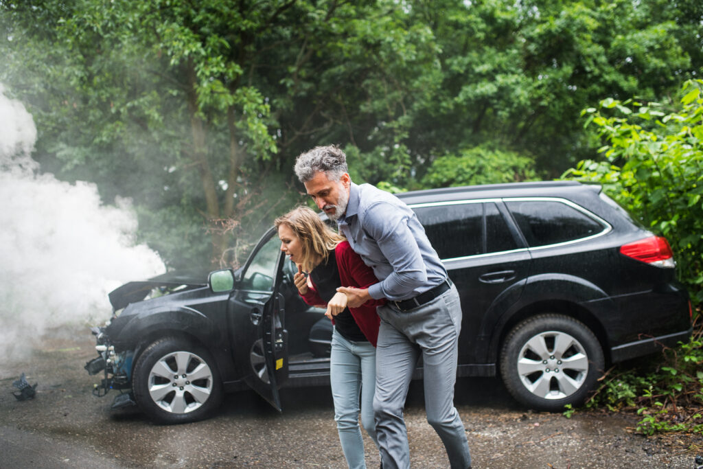 A mature man helping a young woman to walk away from the car after an accident